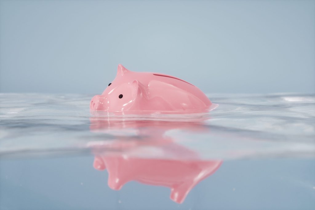 pink piggy bank sinking into water meant to symbolize the value of money sinking